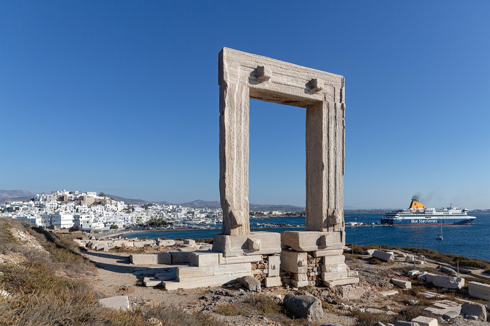 The Portara gateway of Naxos with a ferry passing